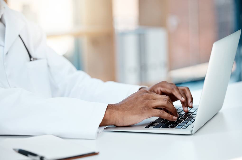 Physician sitting at a desk, typing on a laptop